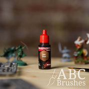 Bottle of the Army Painter Fanatics Wash in the colour Soft Tone with various wargaming models and an ABC paintbrush in the background, on a wooden surface.