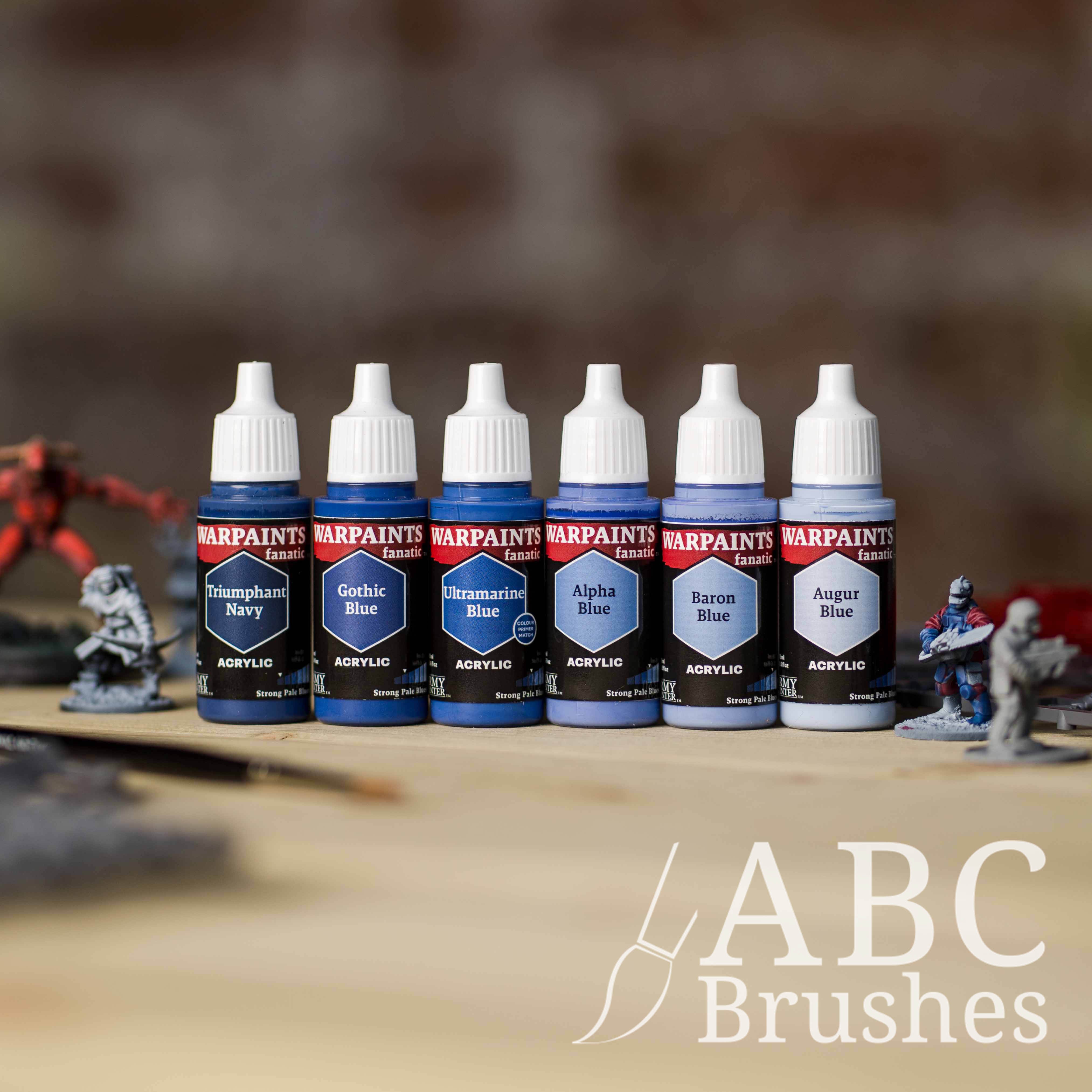 Army Painter Fanatics Strong Pale Blues Triad on a wooden surface. There are wargaming models and an ABC paint brush next to them.