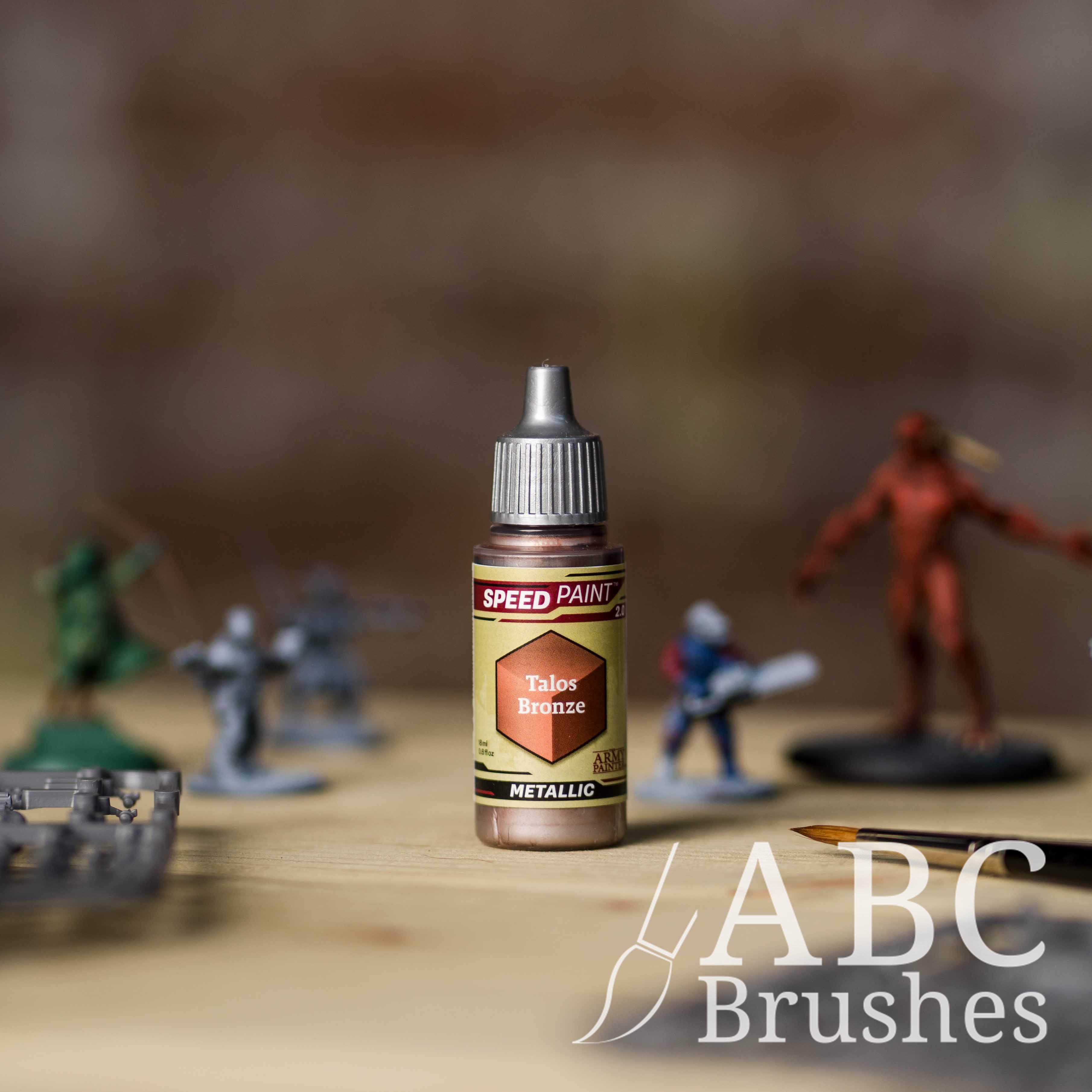 Bottle of the Army Painters Metallic Speedpaint in the colour Talos Bronze, with wargaming models and an ABC paintbrush in the background, on a wooden surface.