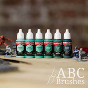Army Painter Fanatics Teals Triad on a wooden surface. There are wargaming models and an ABC paint brush next to them.