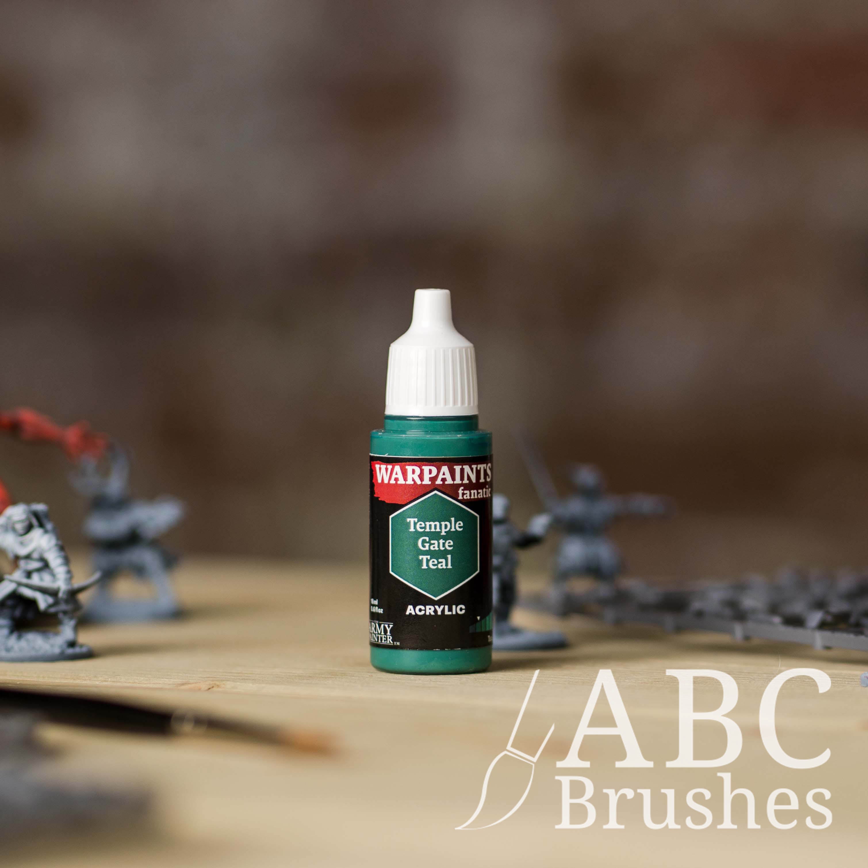 Bottle of the Army Painter Fanatics in the colour Temple Gate Teal with various wargaming models and an ABC paintbrush in the background, on a wooden surface.