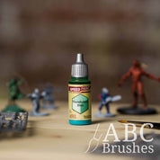 Bottle of the Army Painters Speedpaint in the colour Thunderbird Blue, with wargaming models and an ABC paintbrush in the background, on a wooden surface.