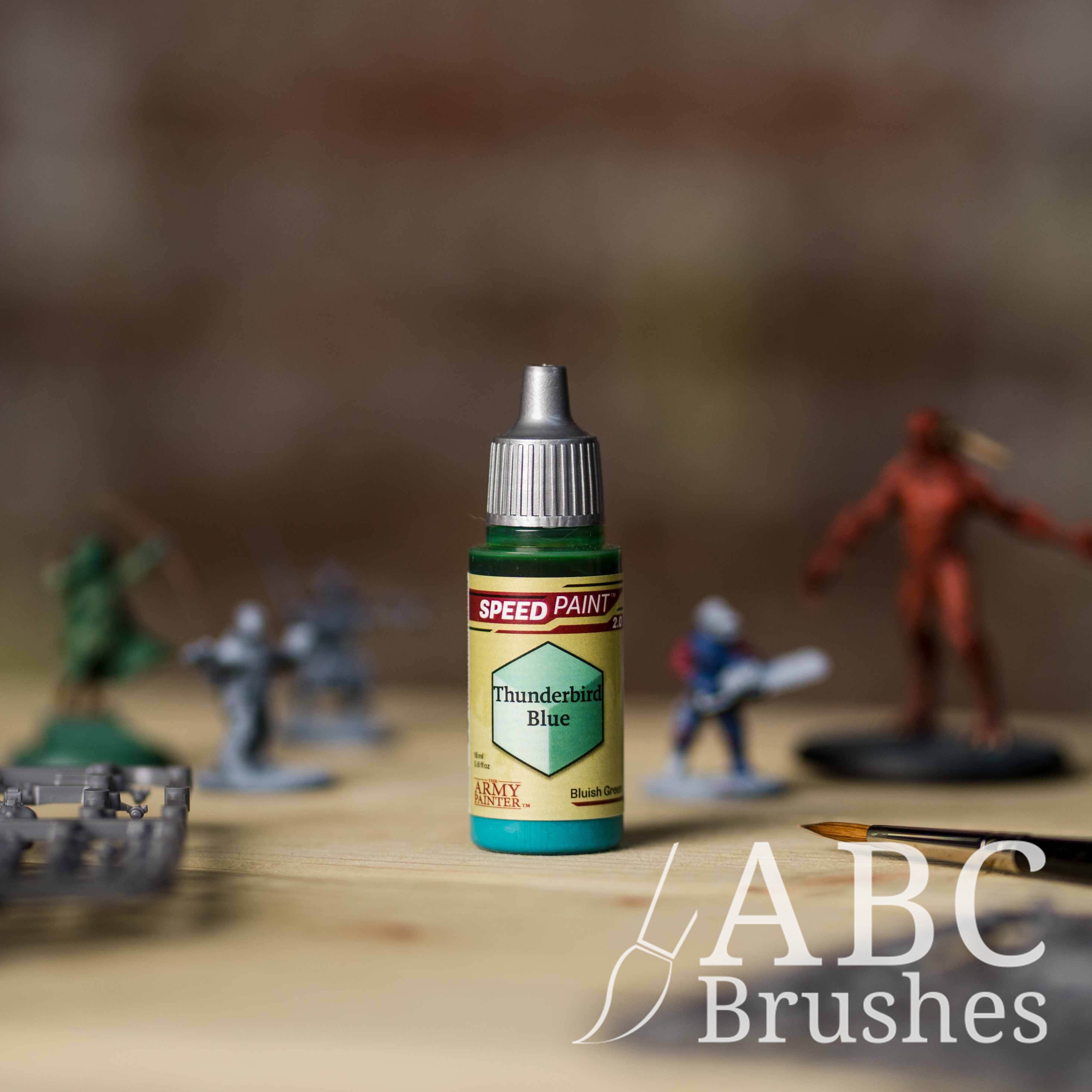 Bottle of the Army Painters Speedpaint in the colour Thunderbird Blue, with wargaming models and an ABC paintbrush in the background, on a wooden surface.
