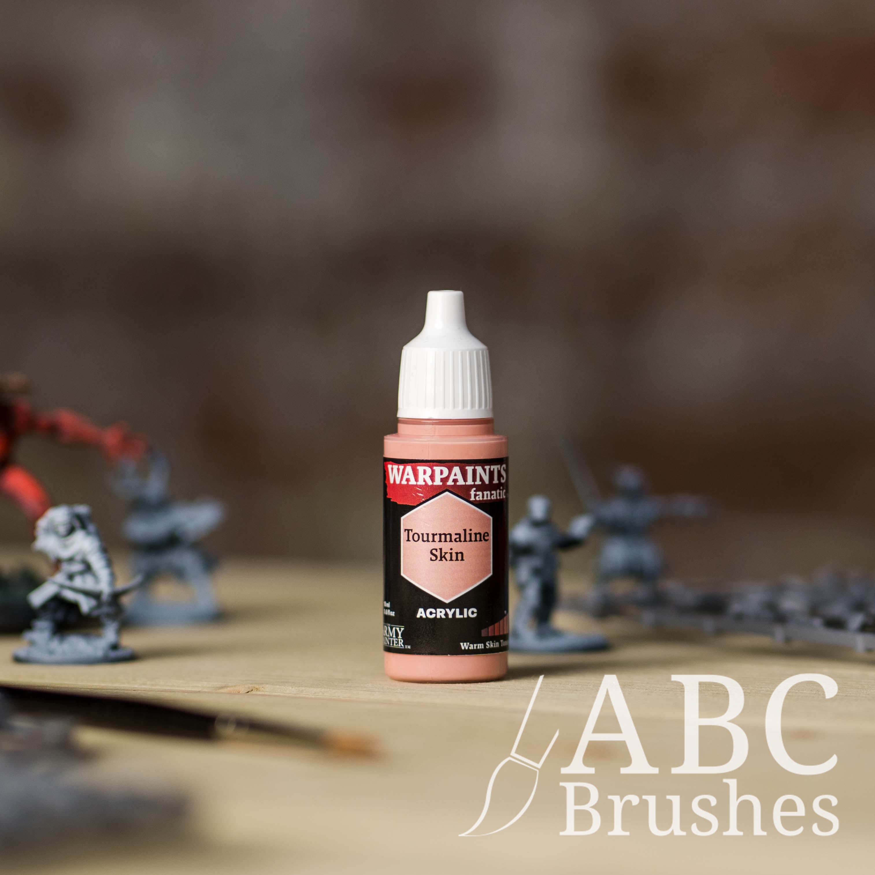 Bottle of the Army Painter Fanatics in the colour Tourmaline Skin with various wargaming models and an ABC paintbrush in the background, on a wooden surface.