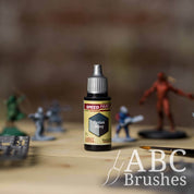 Bottle of the Army Painters Speedpaint in the colour Tyrian Navy, with wargaming models and an ABC paintbrush in the background, on a wooden surface.