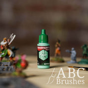 Bottle of the Army Painter Fanatics Effects in the colour Virdigris with various wargaming models and an ABC paintbrush in the background, on a wooden surface.