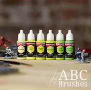 Army Painter Fanatics Vibrant Greens Triad on a wooden surface. There are wargaming models and an ABC paint brush next to them.