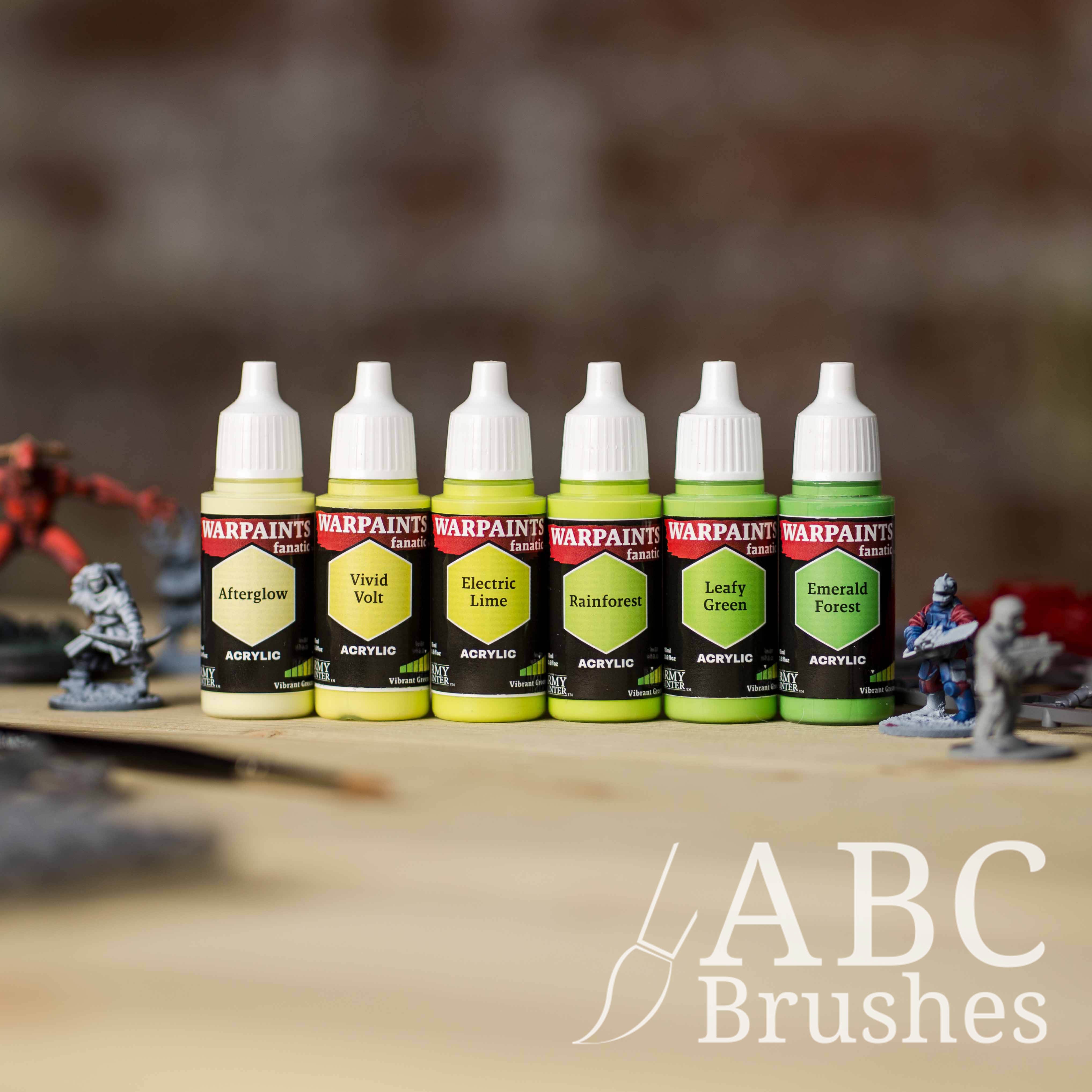 Army Painter Fanatics Vibrant Greens Triad on a wooden surface. There are wargaming models and an ABC paint brush next to them.