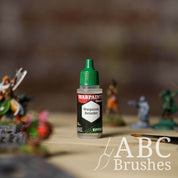 Bottle of the Army Painter Fanatics Effects Warpaints Retarder with various wargaming models and an ABC paintbrush in the background, on a wooden surface.
