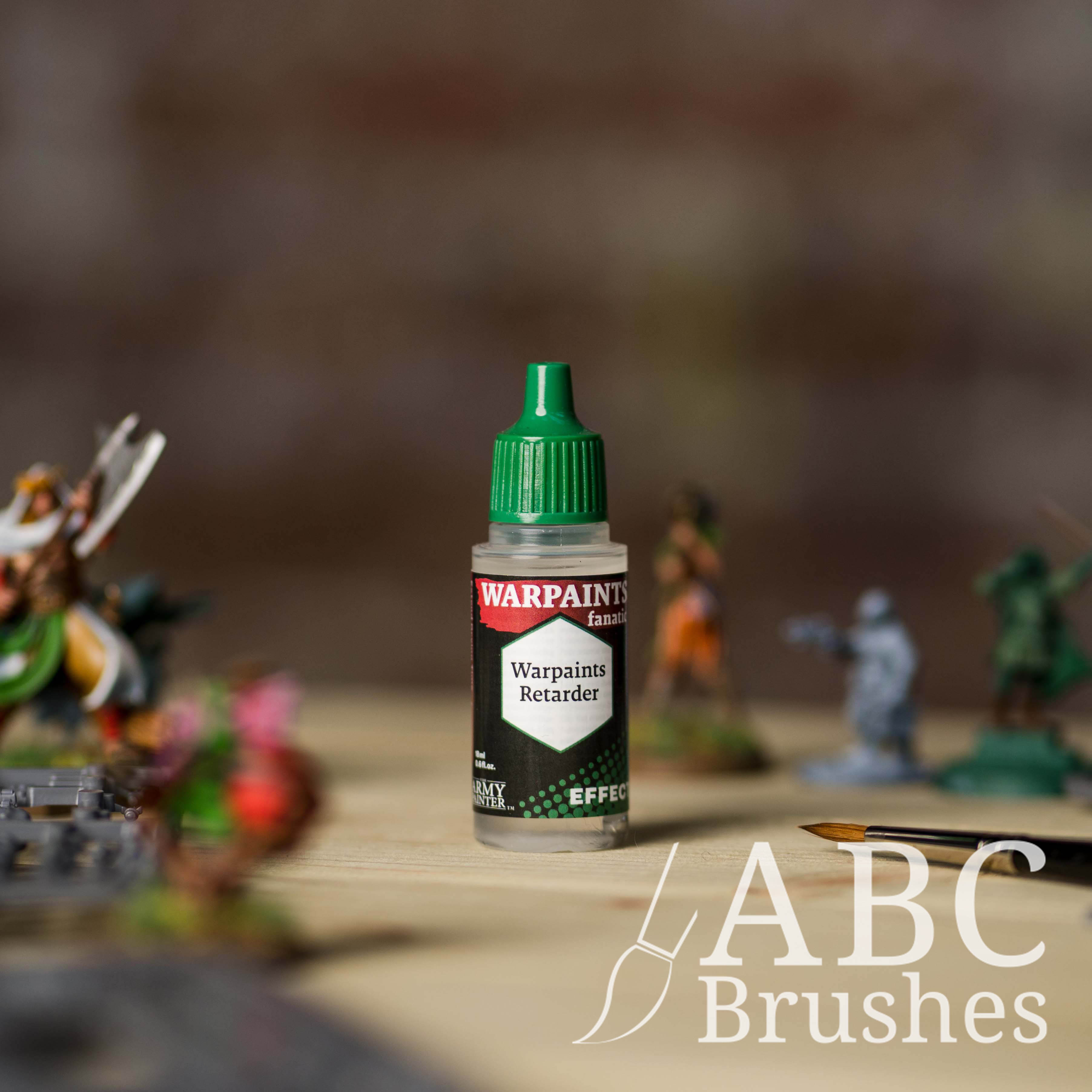 Bottle of the Army Painter Fanatics Effects Warpaints Retarder with various wargaming models and an ABC paintbrush in the background, on a wooden surface.