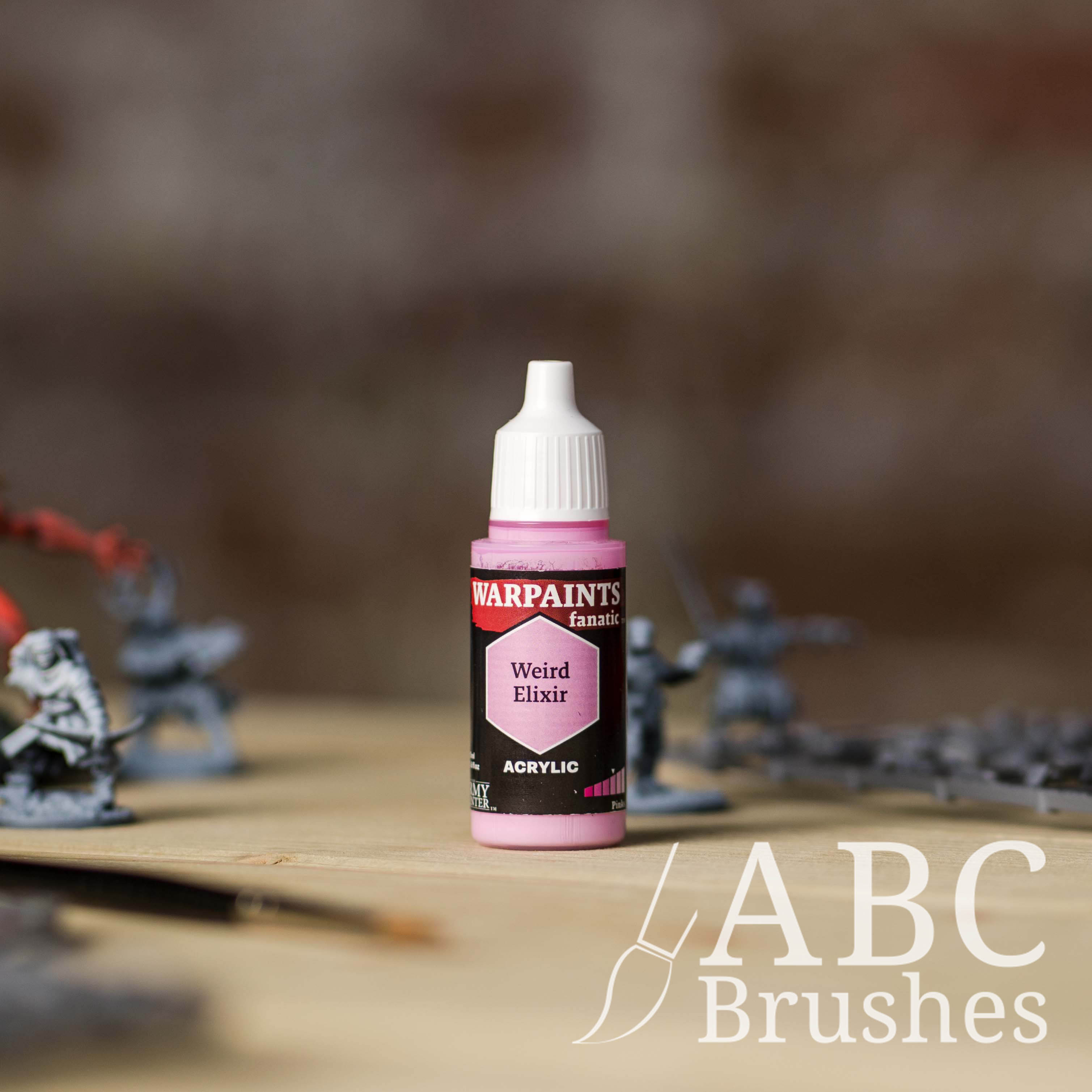 Bottle of the Army Painter Fanatics in the colour Weird Elixir with various wargaming models and an ABC paintbrush in the background, on a wooden surface.