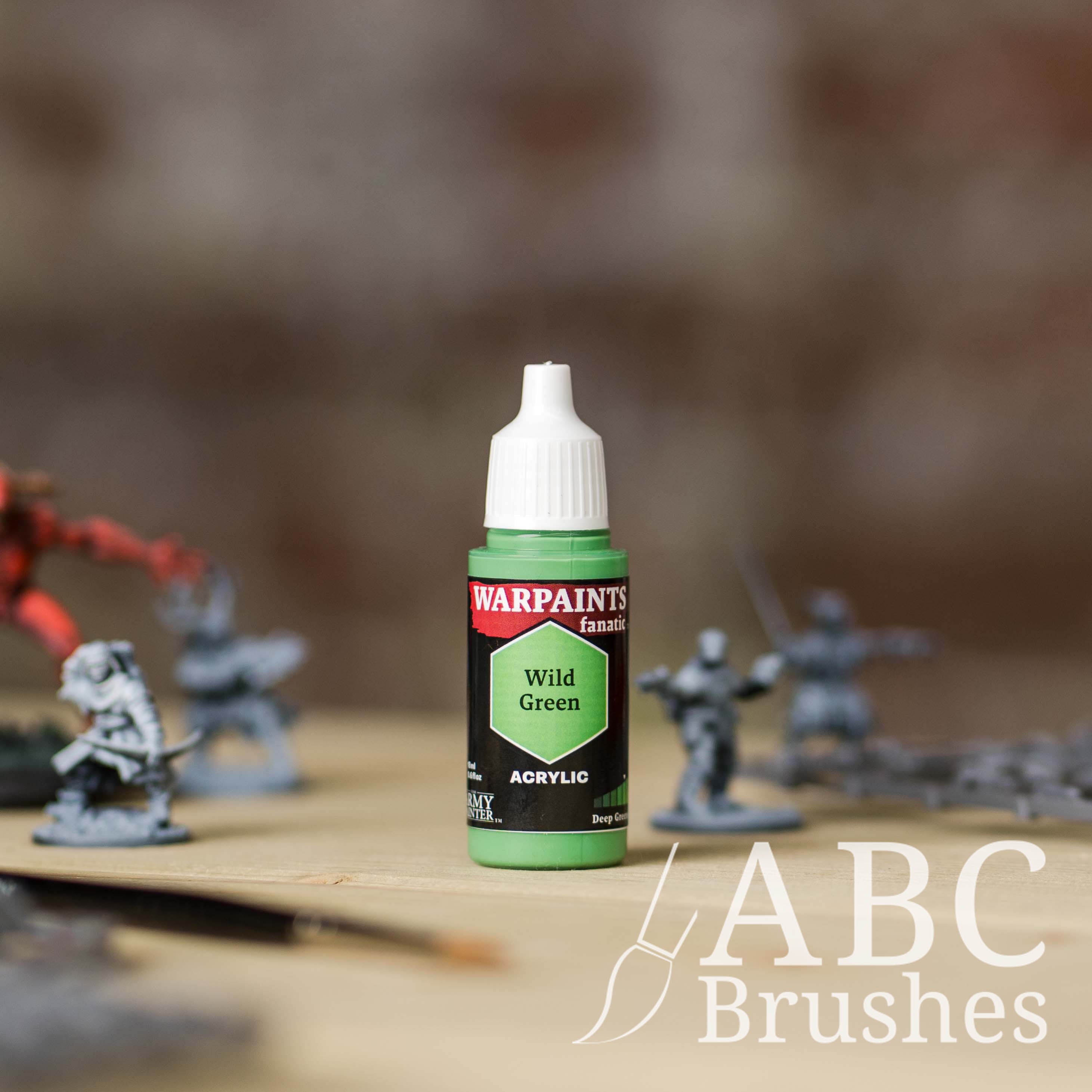 Bottle of the Army Painter Fanatics in the colour Wild Green with various wargaming models and an ABC paintbrush in the background, on a wooden surface.