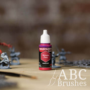 Bottle of the Army Painter Fanatics in the colour Wyvern Fury with various wargaming models and an ABC paintbrush in the background, on a wooden surface.