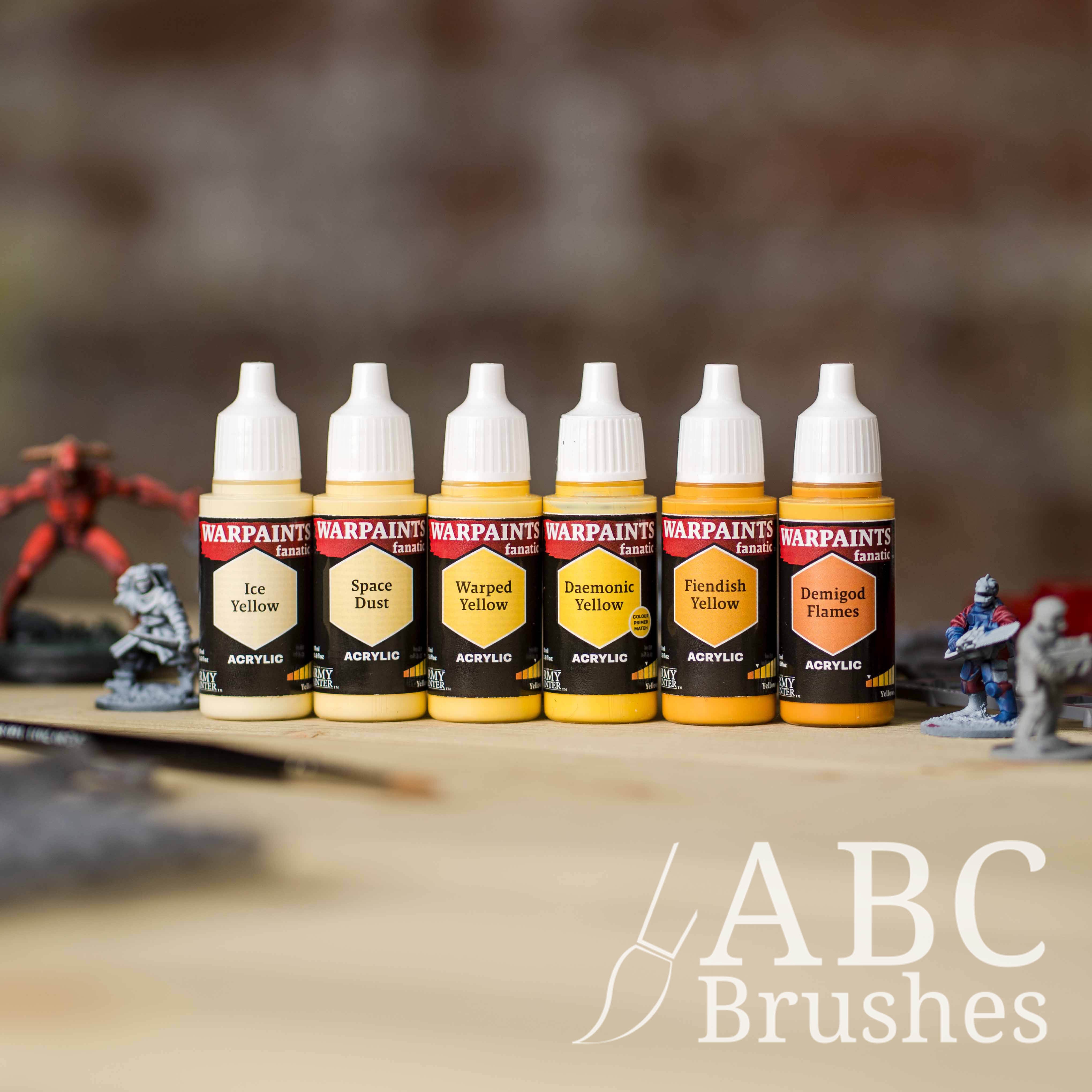 Army Painter Fanatics Yellows Triad on a wooden surface. There are wargaming models and an ABC paint brush next to them.