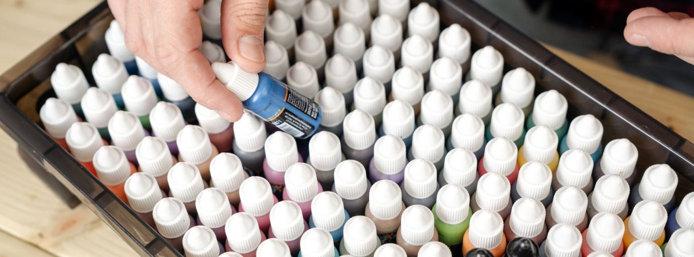 Assorted bottles of acrylic paint in a tray, with one blue paint being picked out. 