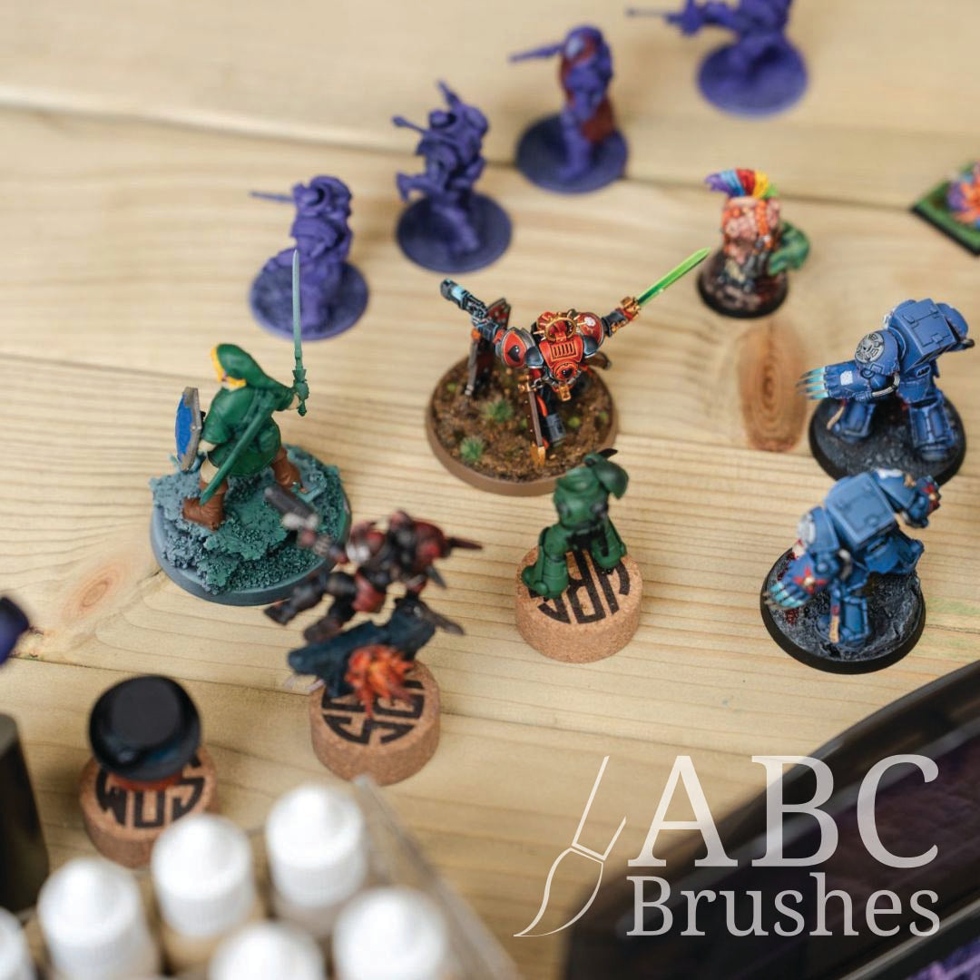 Collection of miniature figurines on a wooden surface in various stages of painting. 