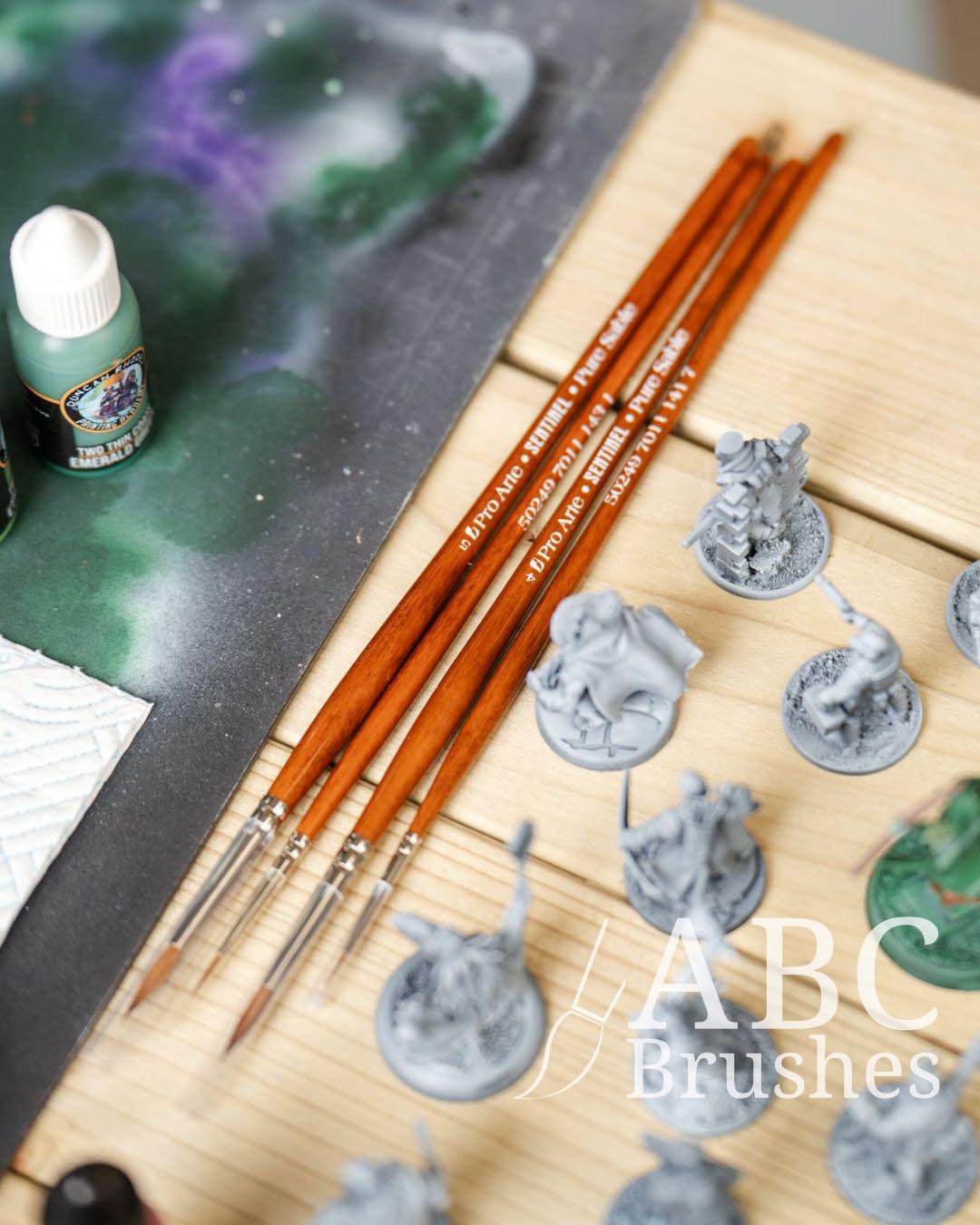 Selection of Pro Arte sentinel brushes, next to various unpainted miniatures and a grey cutting mat. 