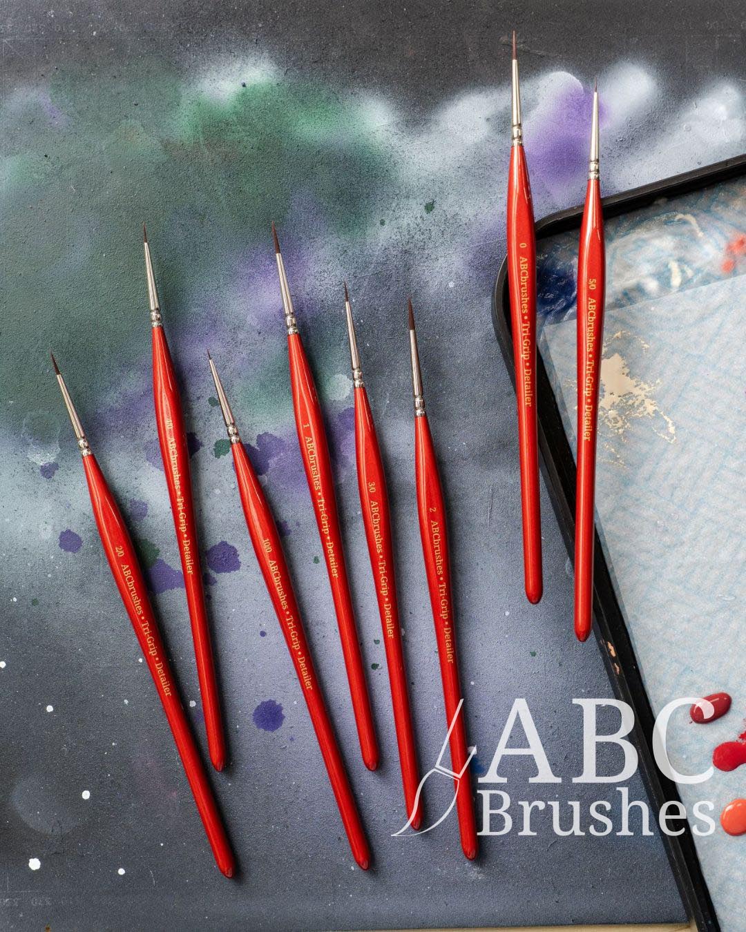 Set of red ABC Sable Spearhead paint brushes on a paint covered cutting mat, with minis next to them. 